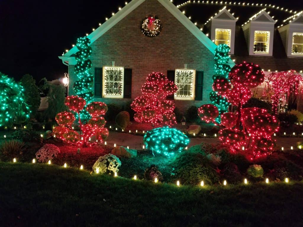 Christmas holiday exterior house with illuminated decorative lights on bushes, trees, and roof.